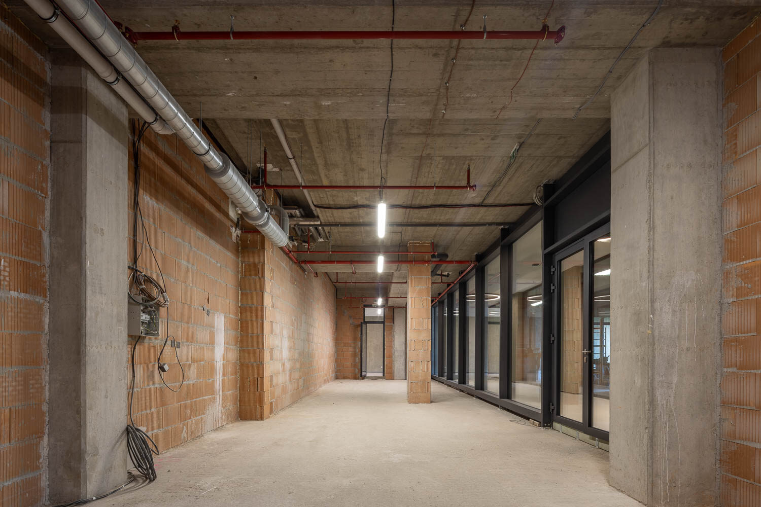 Interiér jednotky ve stavu Shell & Core — pohledový beton, cihlové zdivo, technické rozvody